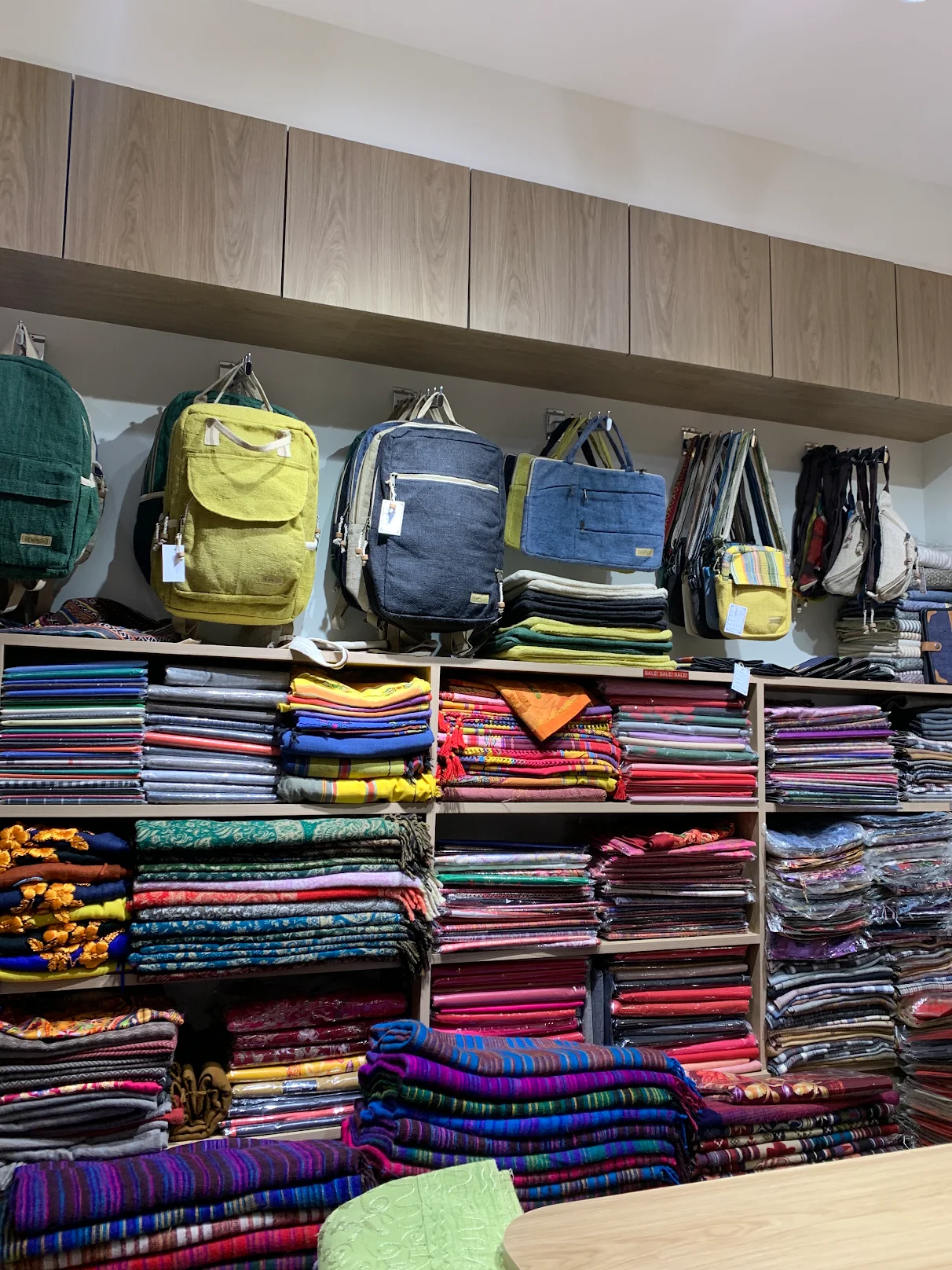 Shelves of folded shawls and blankets under a row of hemp backpacks in the Kedar Craft shop